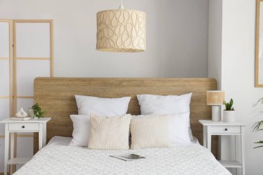 Yatak odasının içinde komodin, lamba, ev bitkileri ve yatak var.