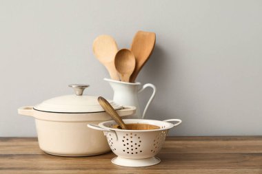 Beyaz duvarın yanındaki masada tencere, kevgir ve ahşap kaplar var.