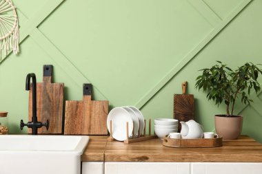 Mutfaktaki yeşil duvarın yanında kesme tahtaları ve bitkileri olan temiz tabaklar.