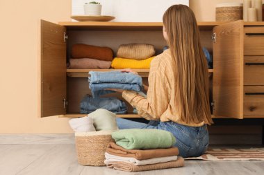 Güzel genç bir kadın, temiz giysileri evdeki dolabına koyuyor.