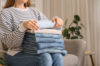 Bir yığın şık elbisesi olan genç bir kadın evdeki kanepede oturuyor.