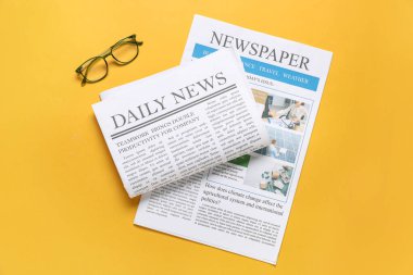 Sarı arka planda gazeteler ve gözlükler. Üst görünüm