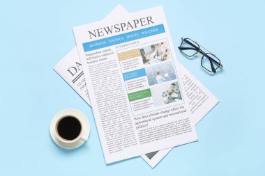 Gazeteler, gözlükler ve mavi arka planda bir fincan kahve. Üst görünüm