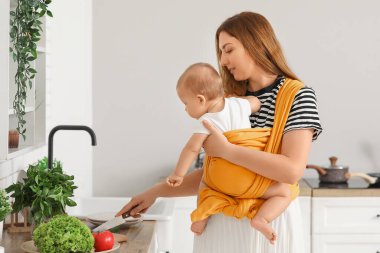 Evde sebze salatası hazırlayan askı küçük bebek ile genç anne