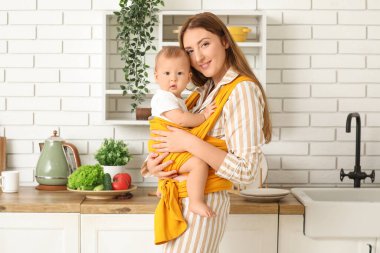 Mutfakta askısında şirin bir bebekle mutlu genç bir anne.