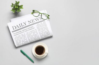 Gözlüklü günlük gazete, bir fincan kahve ve gri arka planda bitki.