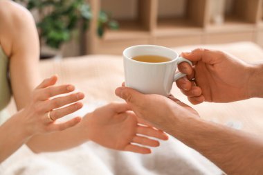 Adam yatak odasındaki kadına bir fincan yeşil çay uzatıyor. Yakın çekim.