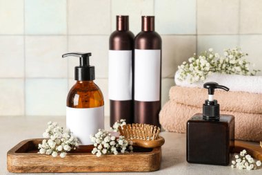 Açık fayans duvarının yanındaki masada şampuan, havlu ve çiçeklerle kompozisyon