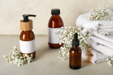 Bej rengi grunge duvarın yanındaki masada şampuan, havlu ve çiçeklerle kompozisyon