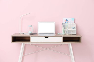 Ofisteki pembe duvarın yanında modern dizüstü bilgisayarı, kırtasiyesi ve lambası olan şık bir iş yeri.