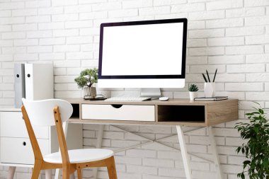 Işık ofisindeki beyaz tuğla duvarın yanında bilgisayar ve sandalye olan şık bir iş yeri