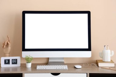 Ofisteki bej duvarın yanında modern bilgisayar, saat ve kırtasiye ile şık bir iş yeri