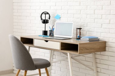 Modern dizüstü bilgisayarı, kulaklığı ve beyaz tuğla duvarın yanındaki koltuğu olan şık bir iş yeri.