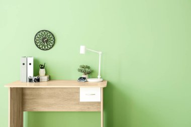 Ofisteki yeşil duvarın yanında klasörleri, lambası ve kırtasiyesi olan şık bir iş yeri