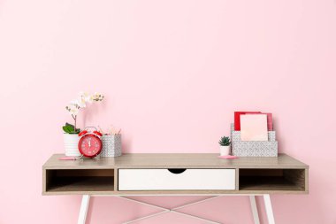 Alarmlı saati, ev bitkisi ve rahat ofisteki pembe duvarın yanındaki defterleri olan şık bir iş yeri.