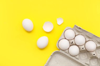 Sarı arka planda tavuk yumurtası ve kabuklu karton kutu.