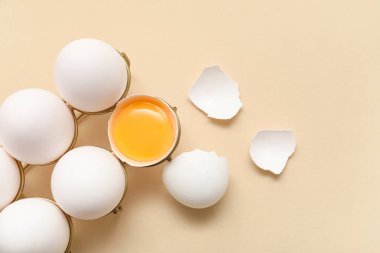 Bej arka planda bütün ve kırılmış tavuk yumurtalarıyla tutucu