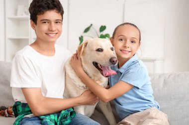 Mutlu kız ve erkek kardeş ve şirin Labrador köpeği evdeki kanepede oturuyor.