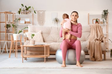 Küçük bebeğiyle evde fitbol oynayan genç bir anne.