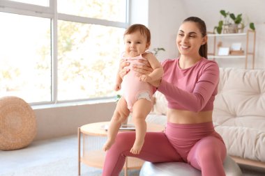 Küçük bebeğiyle evde fitbol oynayan genç bir anne.