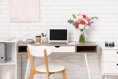 Güzel yıldız çiçekleri ve aydınlatma odasında modern dizüstü bilgisayarı olan şık bir iş yeri.