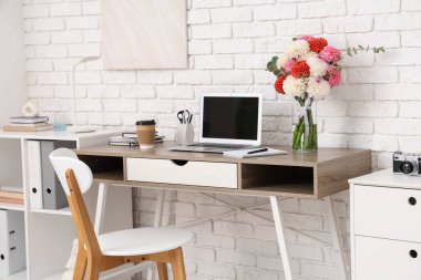 Güzel yıldız çiçekleri ve aydınlatma odasında modern dizüstü bilgisayarı olan şık bir iş yeri.