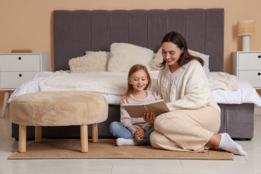 Anne ve küçük kızı yatak odasında oturmuş kitap okuyorlar.