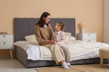 Küçük kız ve annesi sıcak kazaklar içinde yatak odasında oturuyorlar.