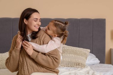 Küçük kız, yatak odasında annesine sarılıyor.