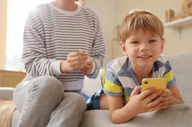 Anne, evdeki koltukta cep telefonu kullanarak oğluna suçiçeği bulaştırıyor.