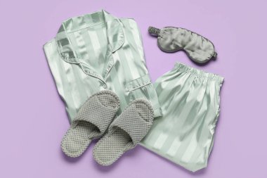 Şık ipek pijamalar, terlikler ve leylak arka planda uyku maskesi.