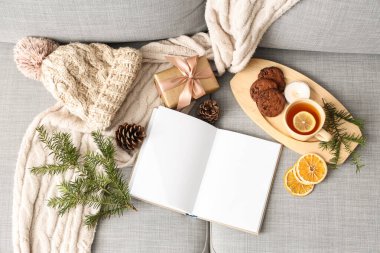 Kışlık aksesuarlı boş kitap, Noel hediyesi ve kanepenin üstünde çay, üst manzara.
