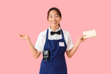 Not defteri, kalem ve ödeme terminali pembe arka planda genç Asyalı gülen garson.