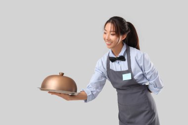 Genç Asyalı gülümseyen garson tepsisi ve gri arka planı ile