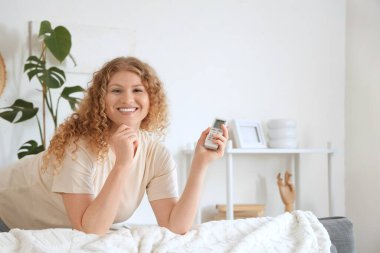 Evinde klimalı uzaktan kumandalı gülümseyen genç bir kadın. Yakın çekim.