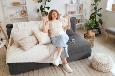 Evdeki kanepede klima kumandalı genç bir kadın.