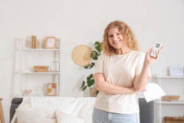 Oturma odasında klima uzaktan kumandalı güzel, gülümseyen genç bir kadın. Yakın çekim.