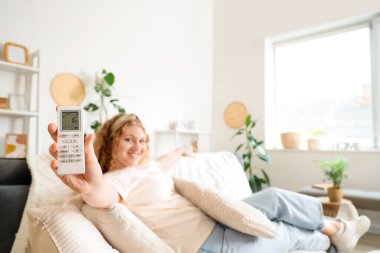 Evinde klima uzaktan kumandalı güzel, gülümseyen genç bir kadın.