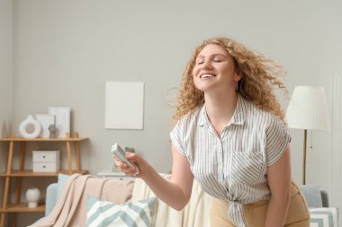 Klimalı, uzaktan kumandalı, evde dinlenen güzel, gülümseyen genç bir kadın. Yakın çekim.