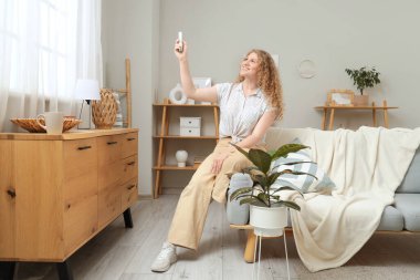 Evinde klima uzaktan kumandalı güzel, mutlu genç bir kadın.