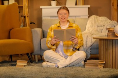 Güzel, genç, mutlu bir kadın akşam evde kitap okuyor.