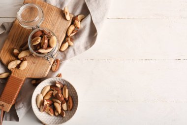 Beyaz ahşap arka planda lezzetli Brezilya fındıkları olan kase ve kavanoz.