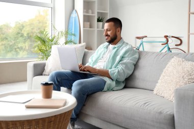 Genç adam kanepede oturan ve dizüstü evde kullanma