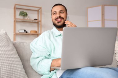 Genç adam cep telefonuyla konuşurken dizüstü bilgisayarla çalışıyor