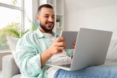 Evde internet işi için tablet ve laptop kullanan genç adam