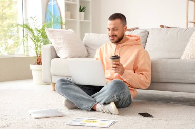 Genç adam dizüstü bilgisayarla çalışıyor ve evde kahve içiyor.