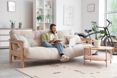 Kulaklık takan, dizüstü bilgisayar kullanan ve evde notlar alan bir serbest yazar.