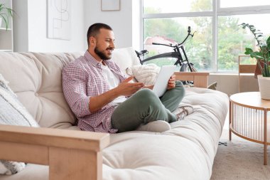 Kanepede oturan ve evde dizüstü bilgisayar kullanan serbest çalışan biri.