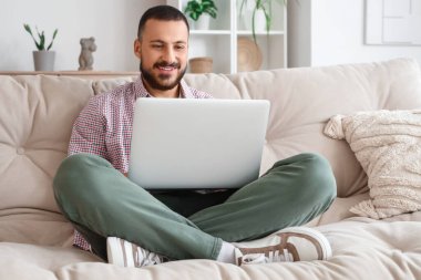 Kanepede oturan ve evde dizüstü bilgisayar kullanan serbest çalışan biri.