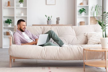 Kanepede yatıp dizüstü bilgisayar kullanan serbest çalışan biri.